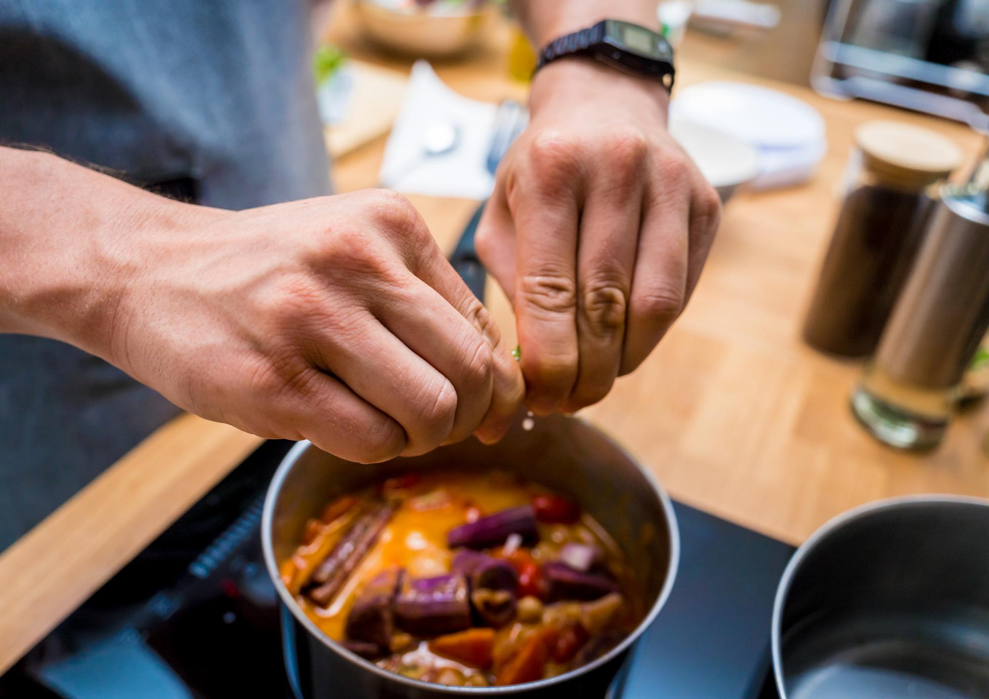 Hands seasoning a skillet while following a recipe card
